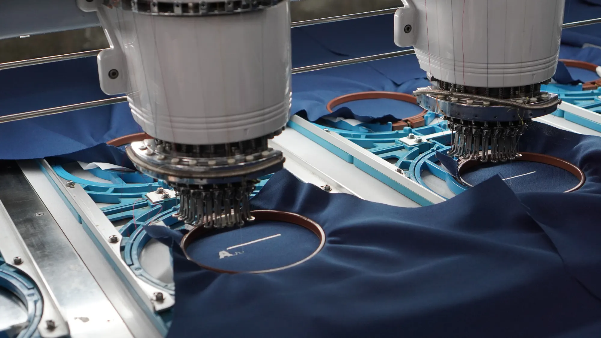 Cabeças da máquina de bordar trabalhando em tecido azul-marinho